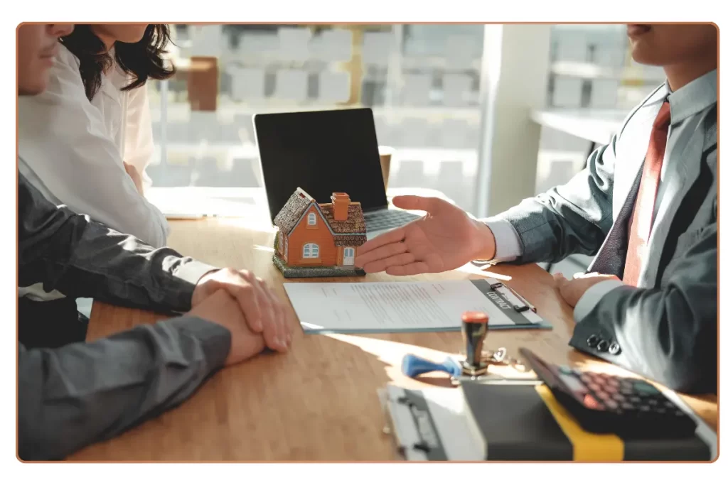 a man and woman sitting at a table with a house model